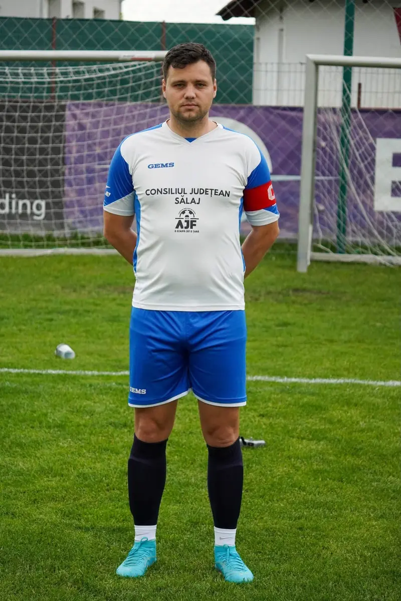 Ortan Vlad pe teren, în echipament alb și albastru, cu banderolă roșie pe braț